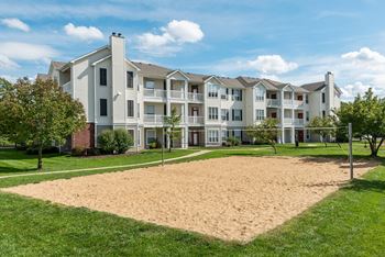 A large sandbox is in the foreground of a building with a green lawn.